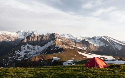 tente rouge sur un champ d'herbe à côté d'une montagne recouverte de glace, photographie de la nature