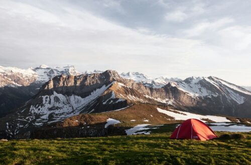 tente rouge sur un champ d'herbe à côté d'une montagne recouverte de glace, photographie de la nature