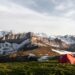 tente rouge sur un champ d'herbe à côté d'une montagne recouverte de glace, photographie de la nature